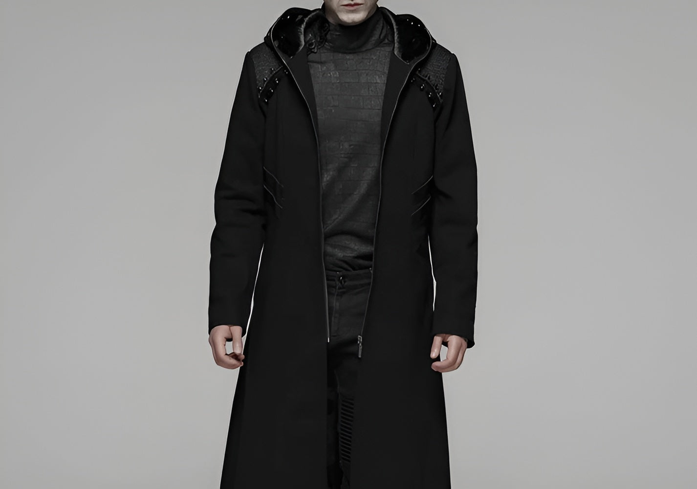 A model wearing a black gothic long coat with studded shoulder details and a hood.