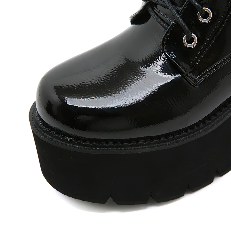 Close-up of women's black patent leather motorcycle ankle boot with metal chain detailing and chunky platform sole.