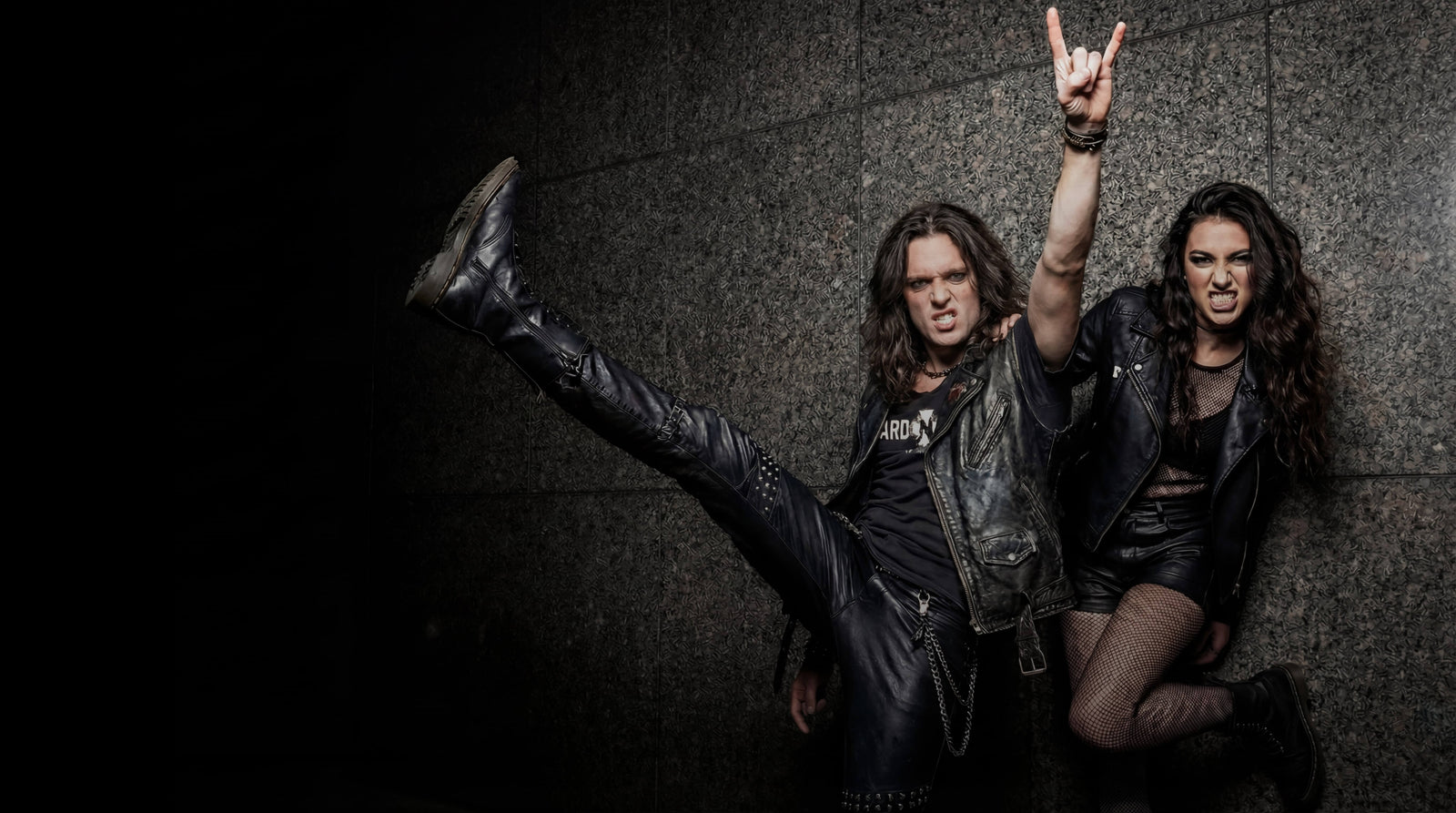 Two people in dark clothing with one kicking out a leg against a dark background