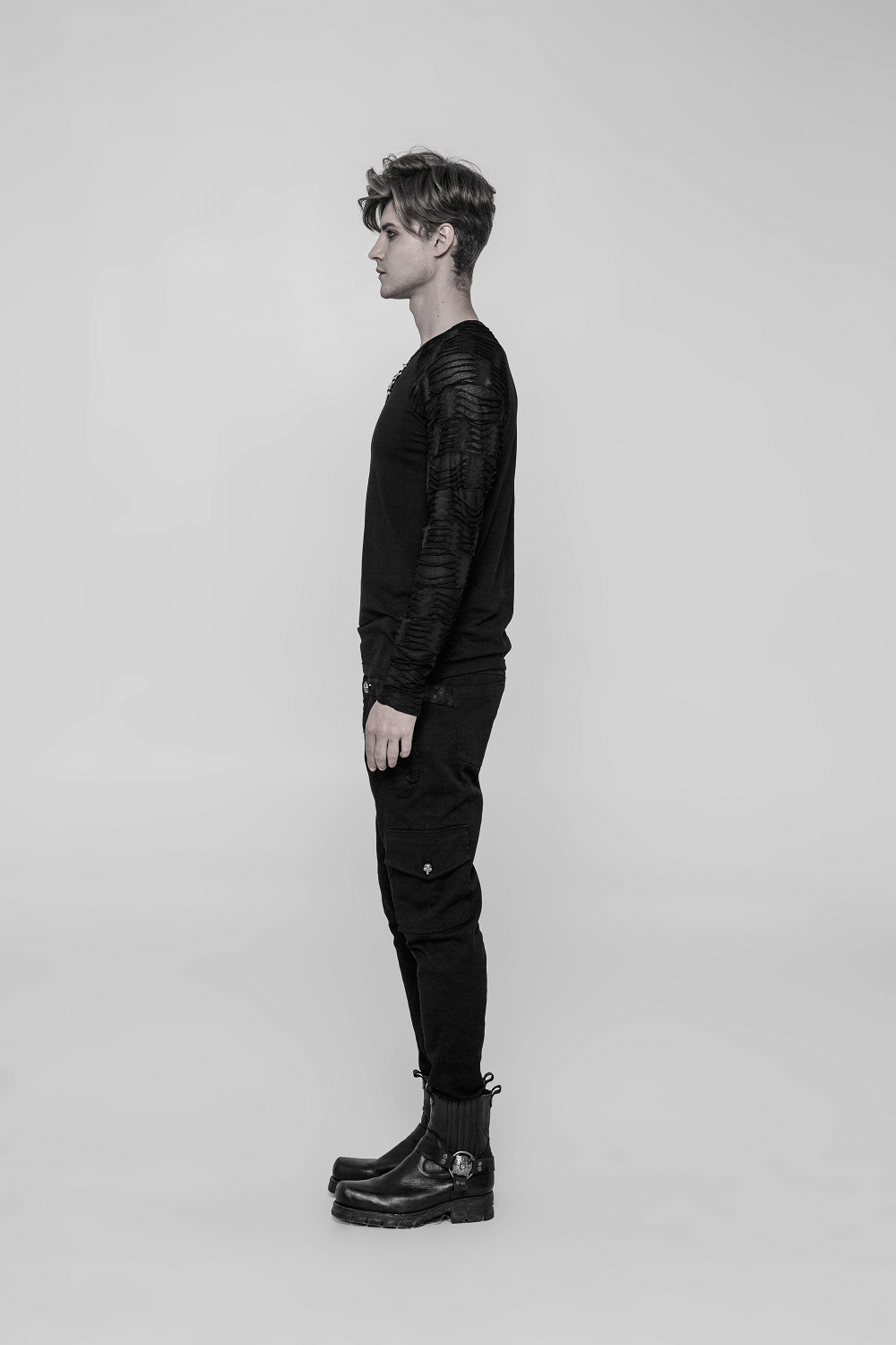 Side view of a man in a black sweatshirt with ripped knit details, paired with black cargo pants and boots.