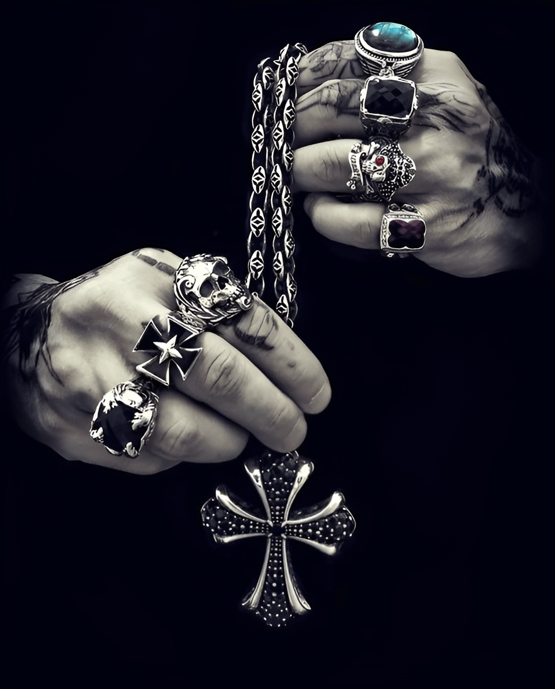 Tattooed hands with silver skull rings and cross pendant.