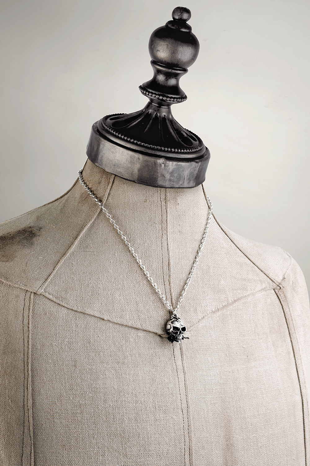 Alchemist skull pendant with black rose accent displayed on a vintage dress form, showcasing gothic metal jewelry style.