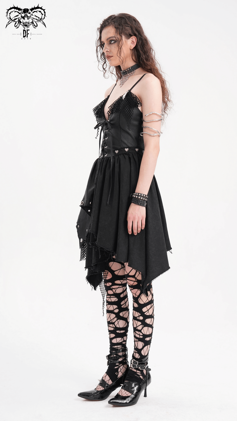 Edgy woman in an asymmetric gothic dress with lace detail and metal accents, styled with bold accessories and fishnet stockings.