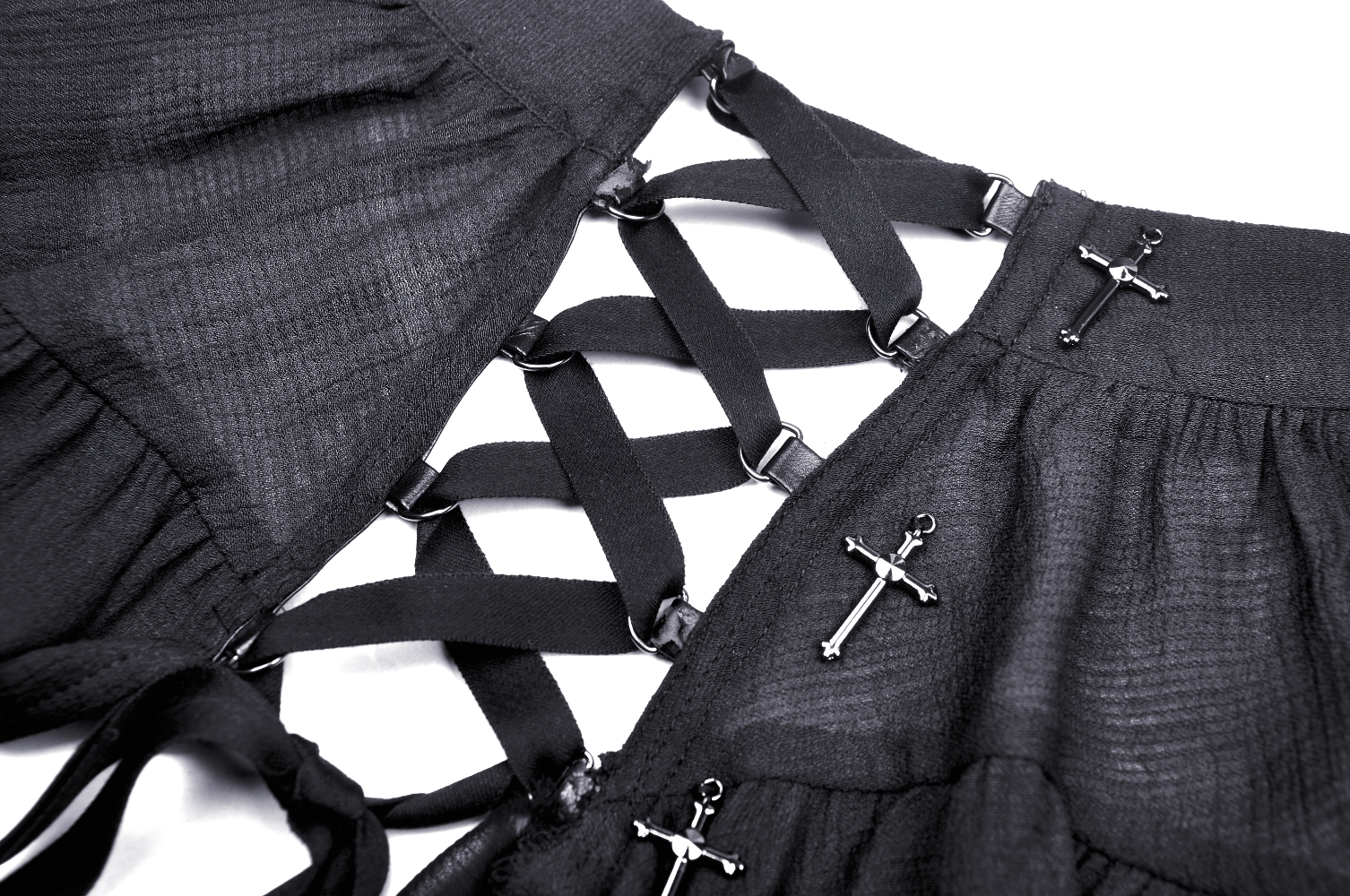 Close-up of black ruffled skirt with crisscross straps and silver cross accents, perfect for punk and gothic fashion.