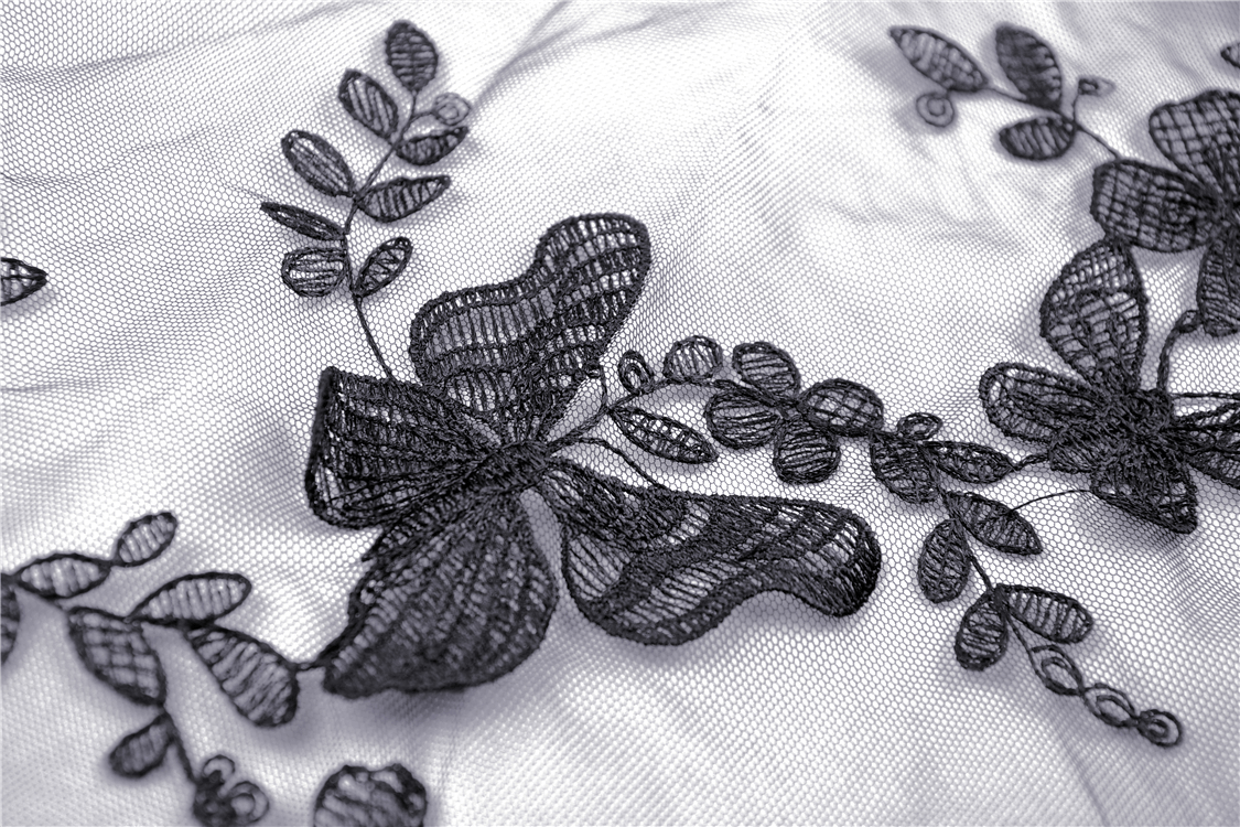 Close-up of intricate black floral embroidery with butterfly designs on sheer fabric.