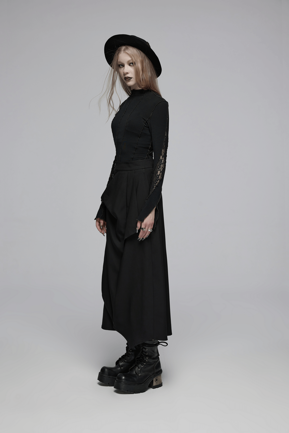 Model in avant-garde asymmetric draped skirt with buckle detail and black long-sleeve top, showcasing edgy fashion style.
