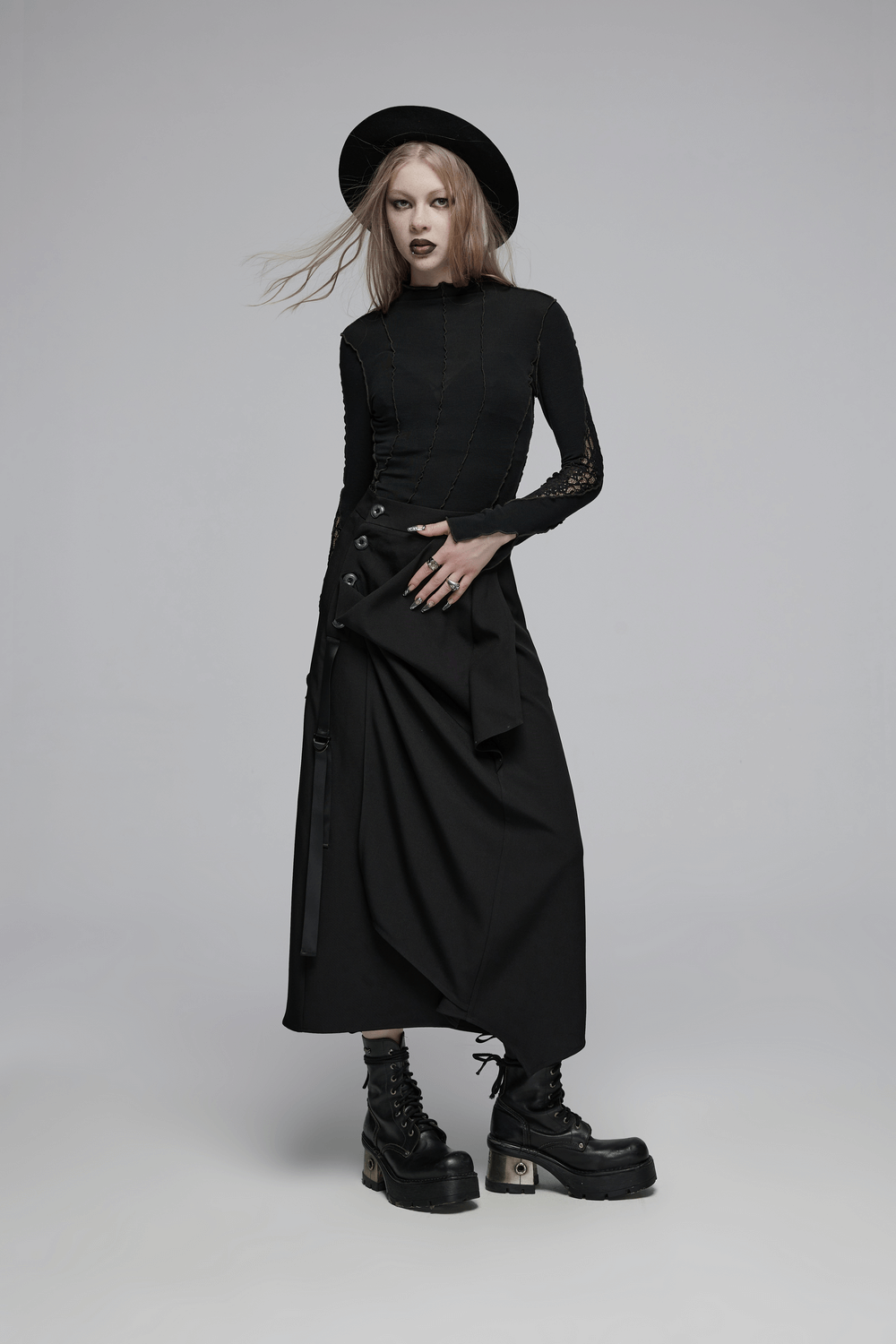 Avant-garde fashion model in black asymmetric drape skirt with buckle detail, paired with chunky boots and a stylish hat.