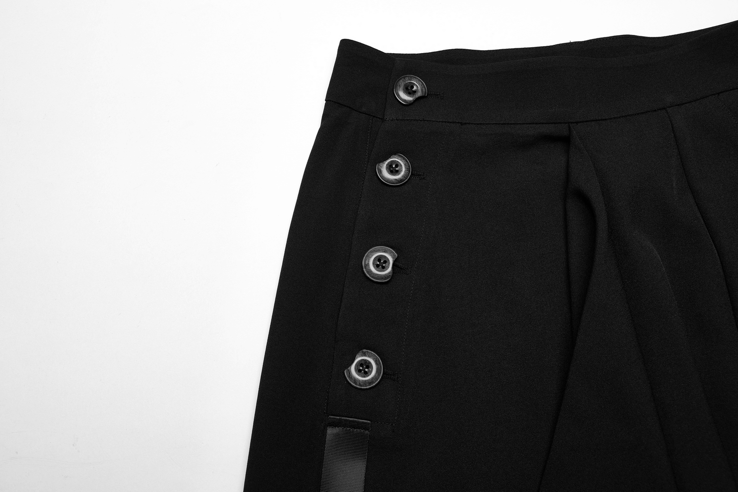 Close-up of black asymmetric skirt showcasing buttons and sleek fabric for a chic, edgy look.