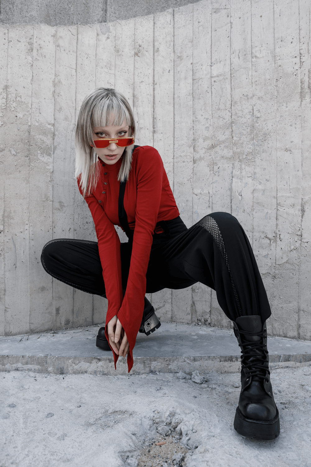 Model posing in avant-garde black wide-leg pants and red top, showcasing fashionable street style with edgy accessories.