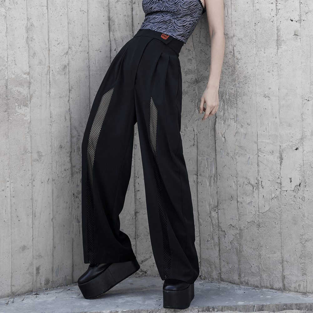 Avant-garde black high-waisted wide-leg pants with mesh details and removable straps, styled on model against a concrete backdrop.