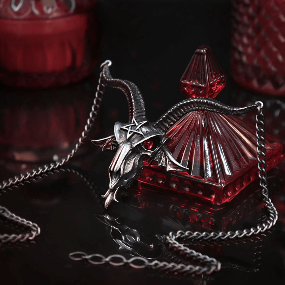Baphomet skull necklace with red crystal eyes, set against a dark backdrop with gothic decor.