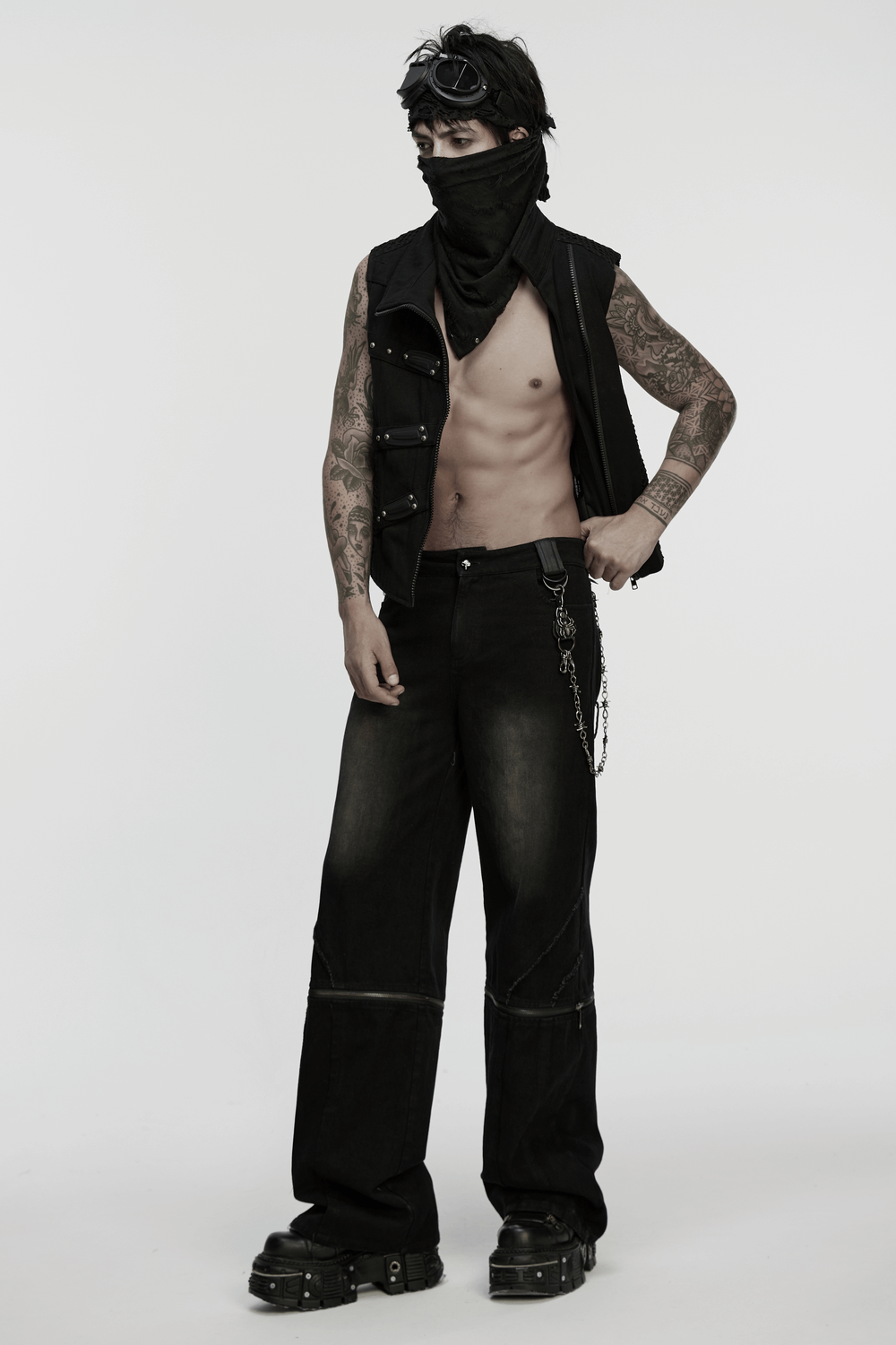 Stylish punk model wearing a black vest and baggy pants, showcasing tattoos and a rebellious look.