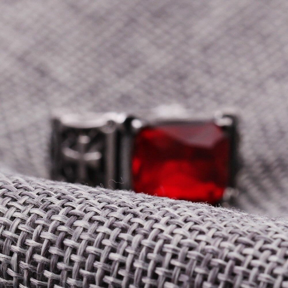 Close-up of a biker stainless steel ring featuring a large red CZ zircon on textured gray fabric.
