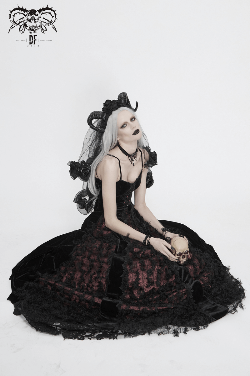 Model in a black and red gothic velvet long dress with lace details, sitting elegantly against a white background.