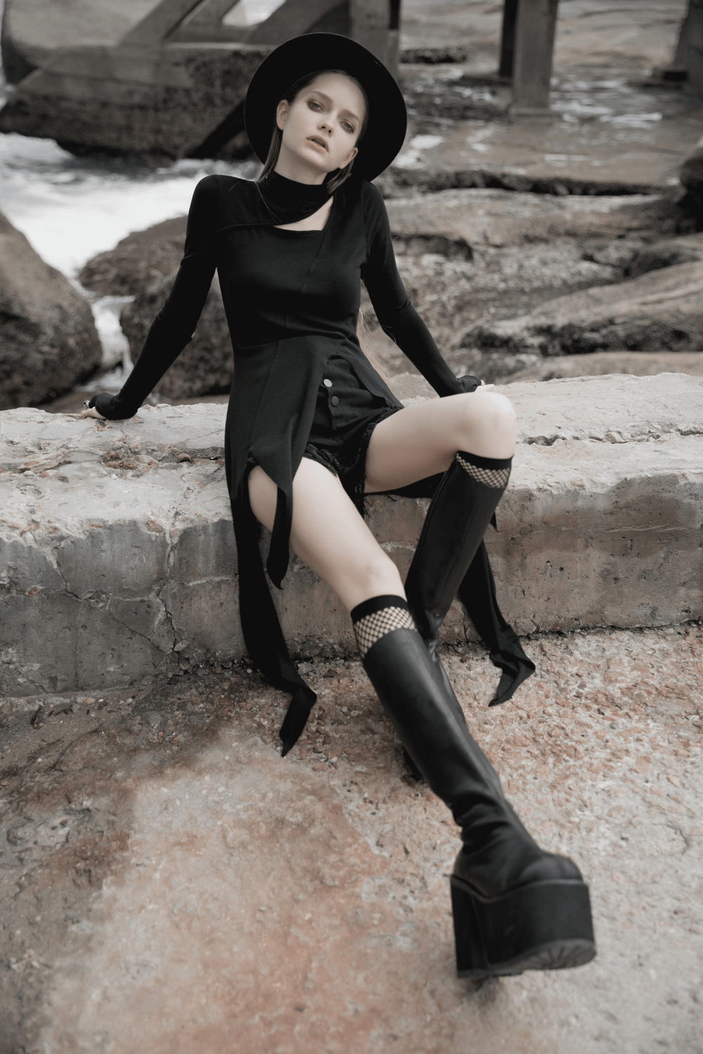 Model showcasing a chic black asymmetric knit dress with sleeve cut-outs and bold thigh-high boots, exuding edgy style.