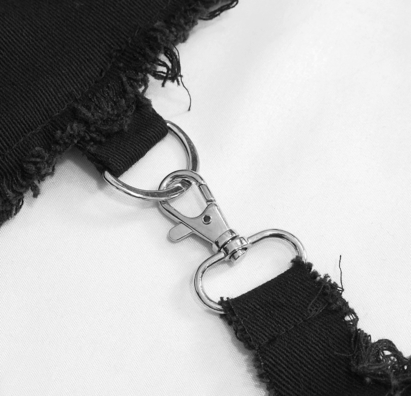 Close-up of silver clasp detail on black asymmetrical pants, showcasing gothic style design elements.