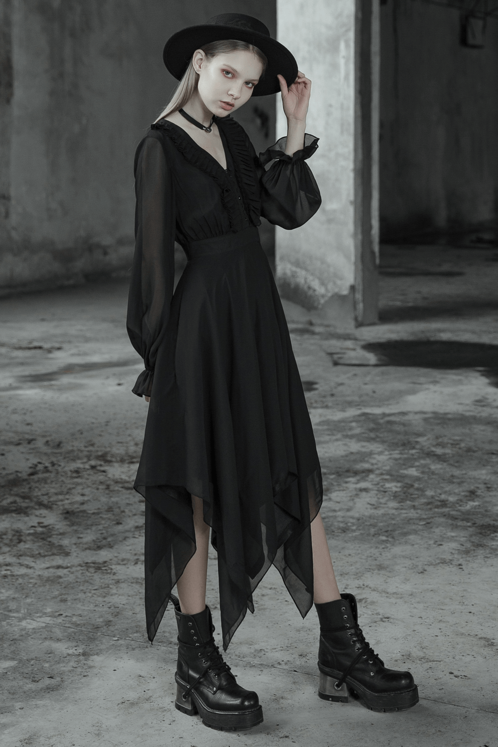 Elegant black chiffon dress with asymmetrical hem, paired with a stylish hat and edgy boots in a moody setting.