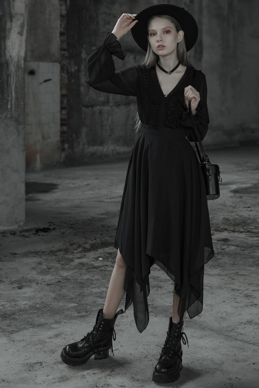 Stylish woman in a black chiffon dress with asymmetrical hem and gothic details, paired with chunky boots and hat.