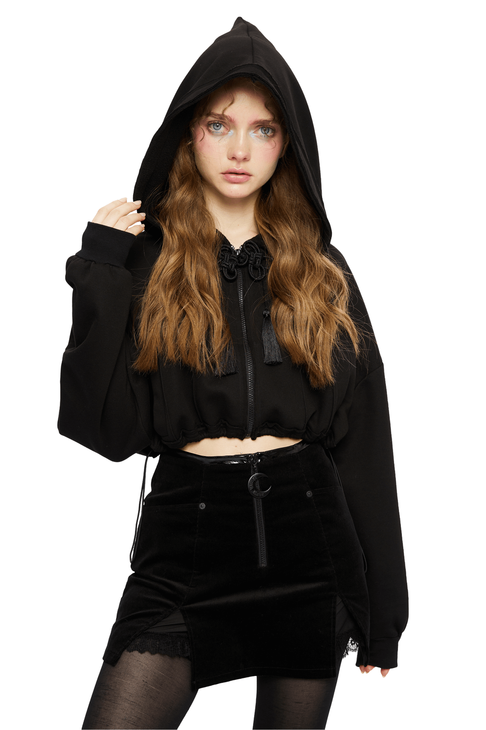 Black cropped hoodie with wizard hood, featuring tassel details and adjustable drawstring, styled with a chic skirt.