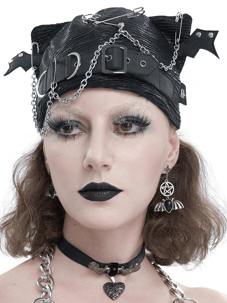Edgy black batwing buckle hat with chains and pins, worn by a model in gothic style makeup and jewelry.