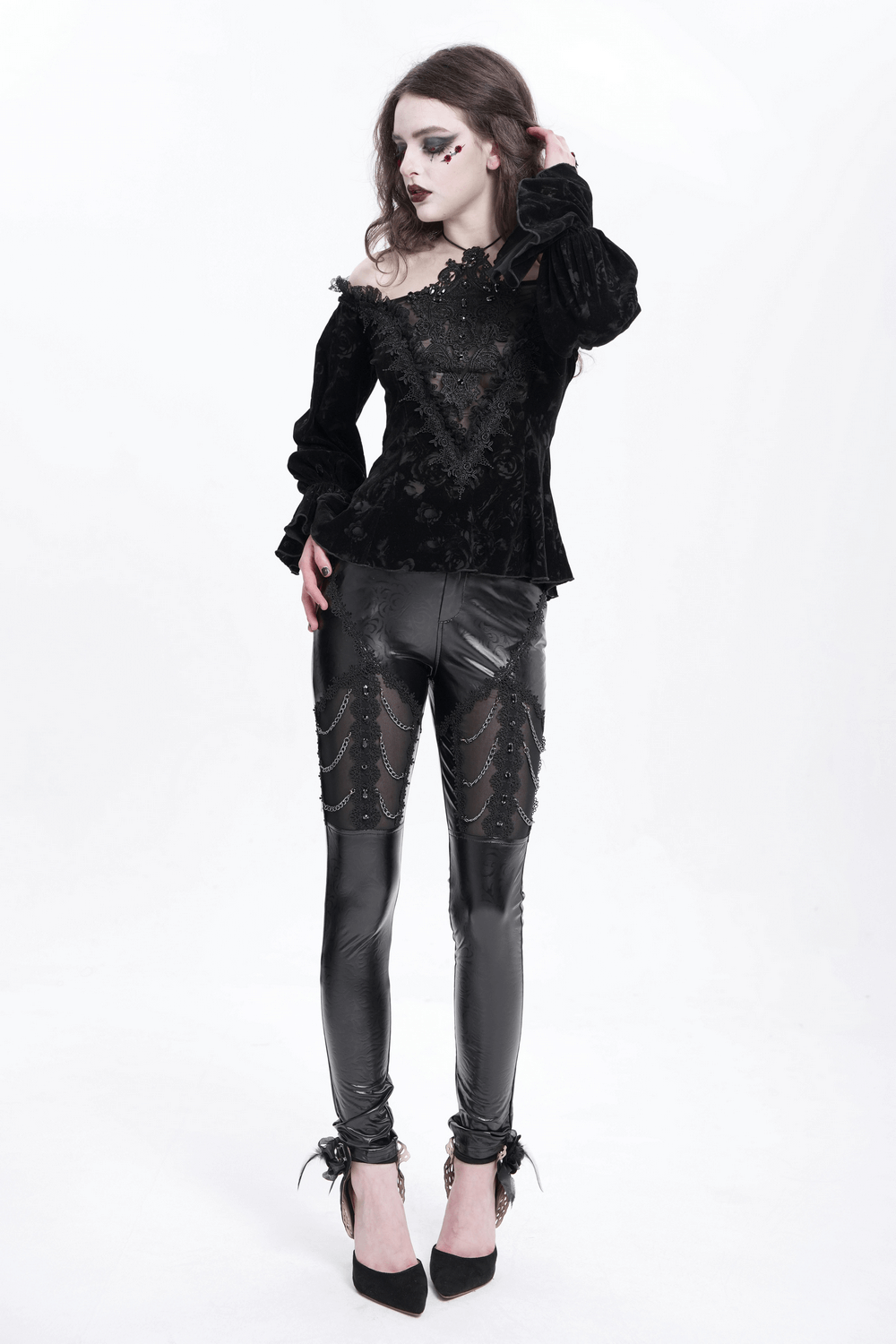 Model wearing black faux leather pants with chains and sequins, paired with a stylish black top in a goth-inspired look.