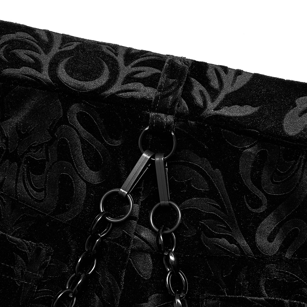 Close-up of black floral velvet fabric with chains on flared pants, adding a gothic touch to a stylish outfit.