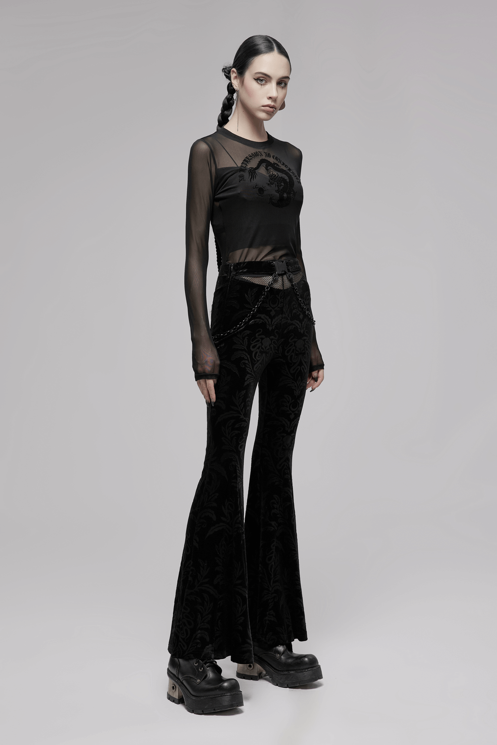 Gothic model showcasing black floral velvet flared pants with chains and mesh waist, exuding dark elegance.