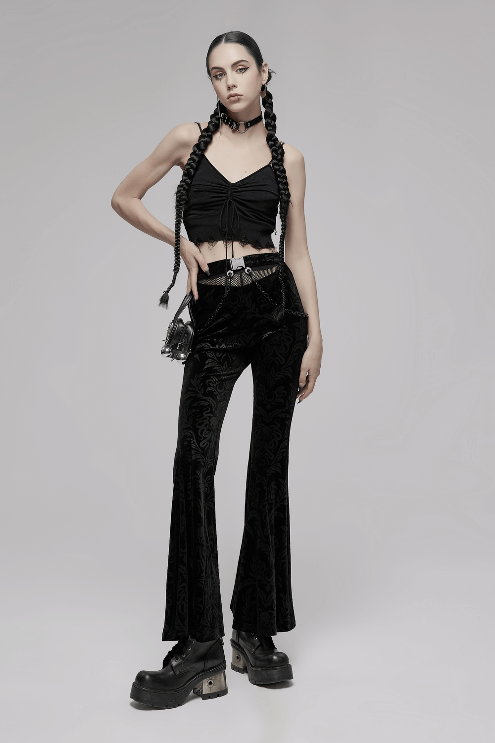 Model wearing black floral velvet flared pants with chains and mesh waist, styled with a cropped black top.