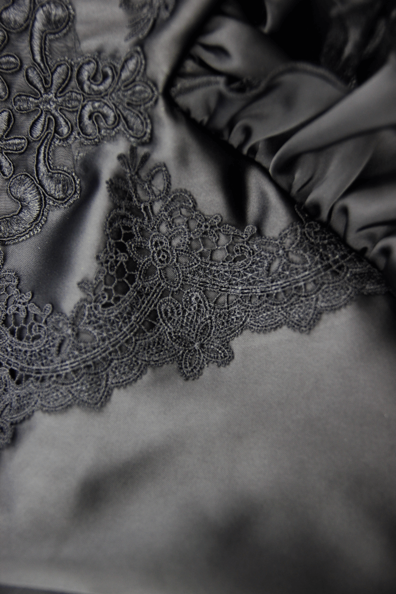 Close-up of intricate lace detailing on a black satin fabric, showcasing gothic elegance and luxurious texture.