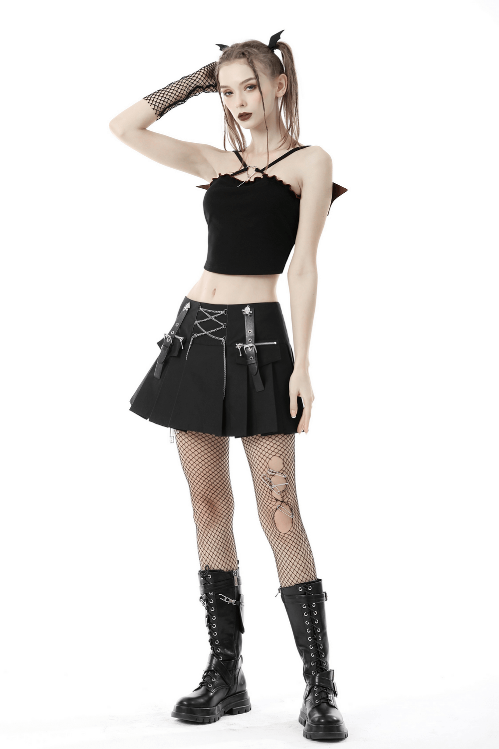 Edgy model in black batwing crop top, pleated skirt, fishnet stockings, and combat boots, showcasing punk rock fashion.