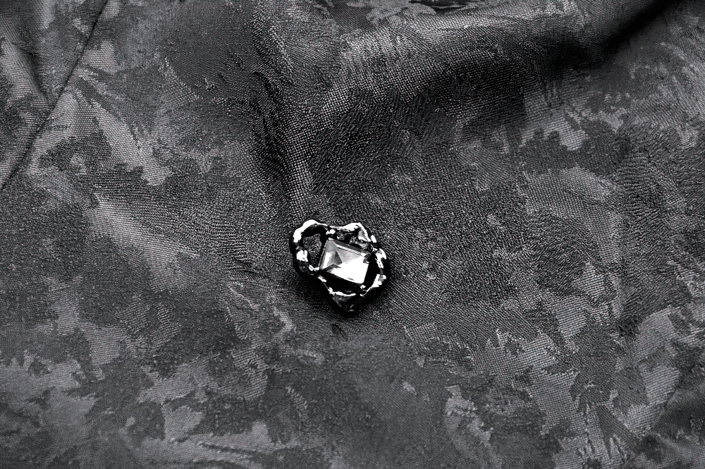 Close-up of a black gem brooch on a textured jacquard fabric featuring an elegant gothic design.