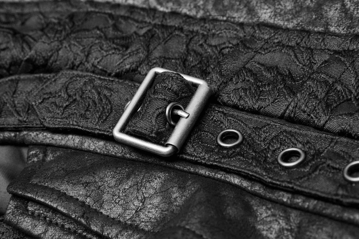 Close-up of a black gothic jacquard waistcoat buckle accent with textured fabric and eyelet details.