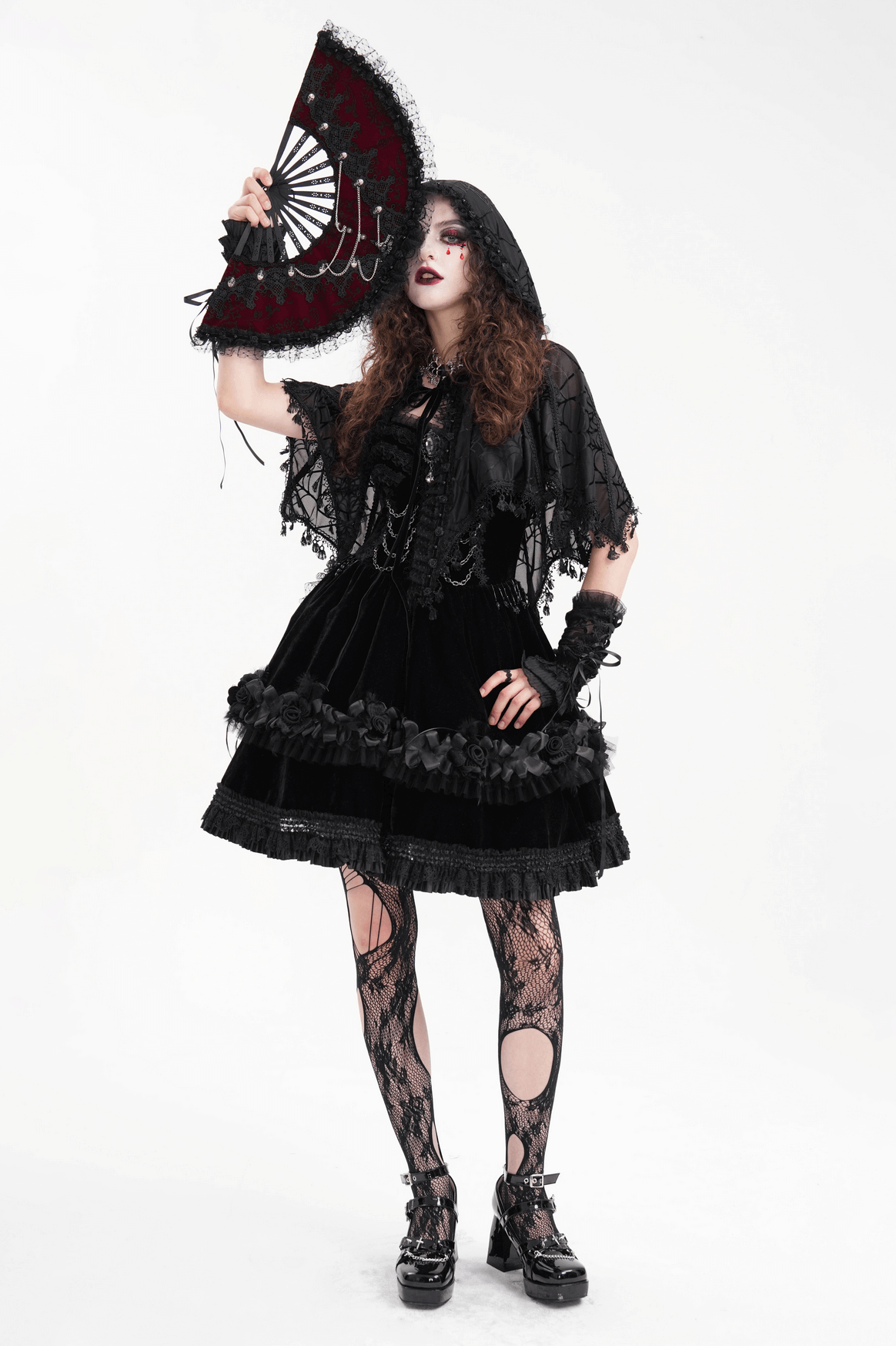 Chic woman in black gothic lace cape with hood, holding a fan, showcasing a striking dark fashion style.