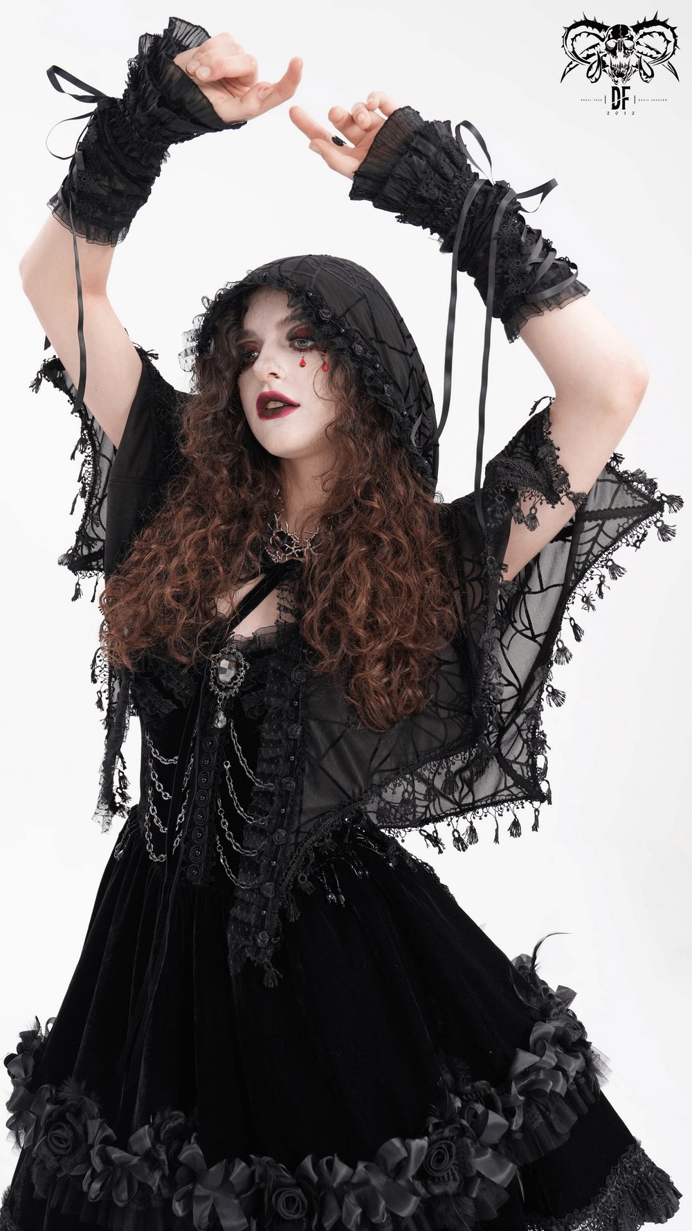 Woman wearing a black gothic lace cape with hood, showcasing a dramatic spiderweb pattern and flowing tassels.