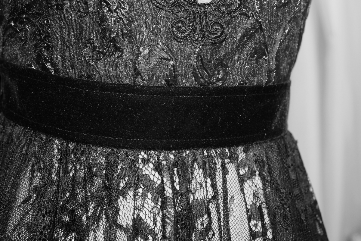 Close-up of elegant black lace dress detail with a velvet waistband, showcasing Gothic style and intricate textures.