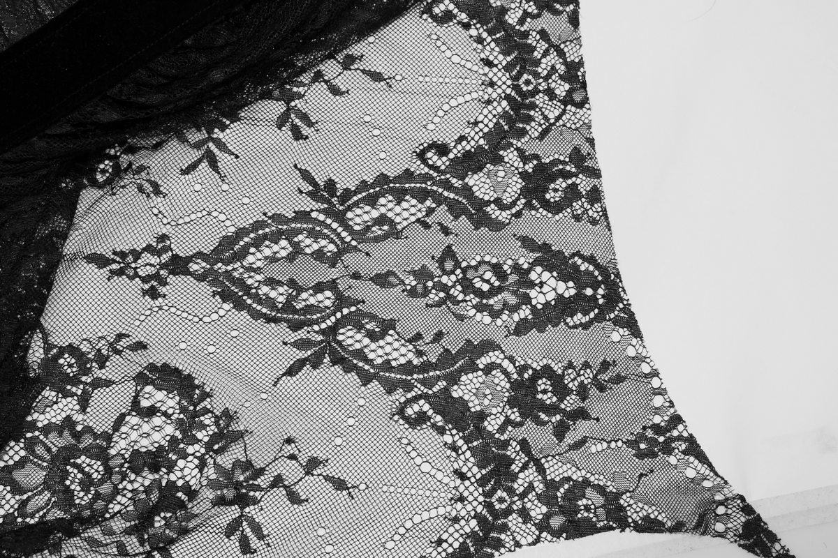 Close-up of elegant black lace detailing on a gothic sleeveless dress, showcasing intricate patterns and texture.