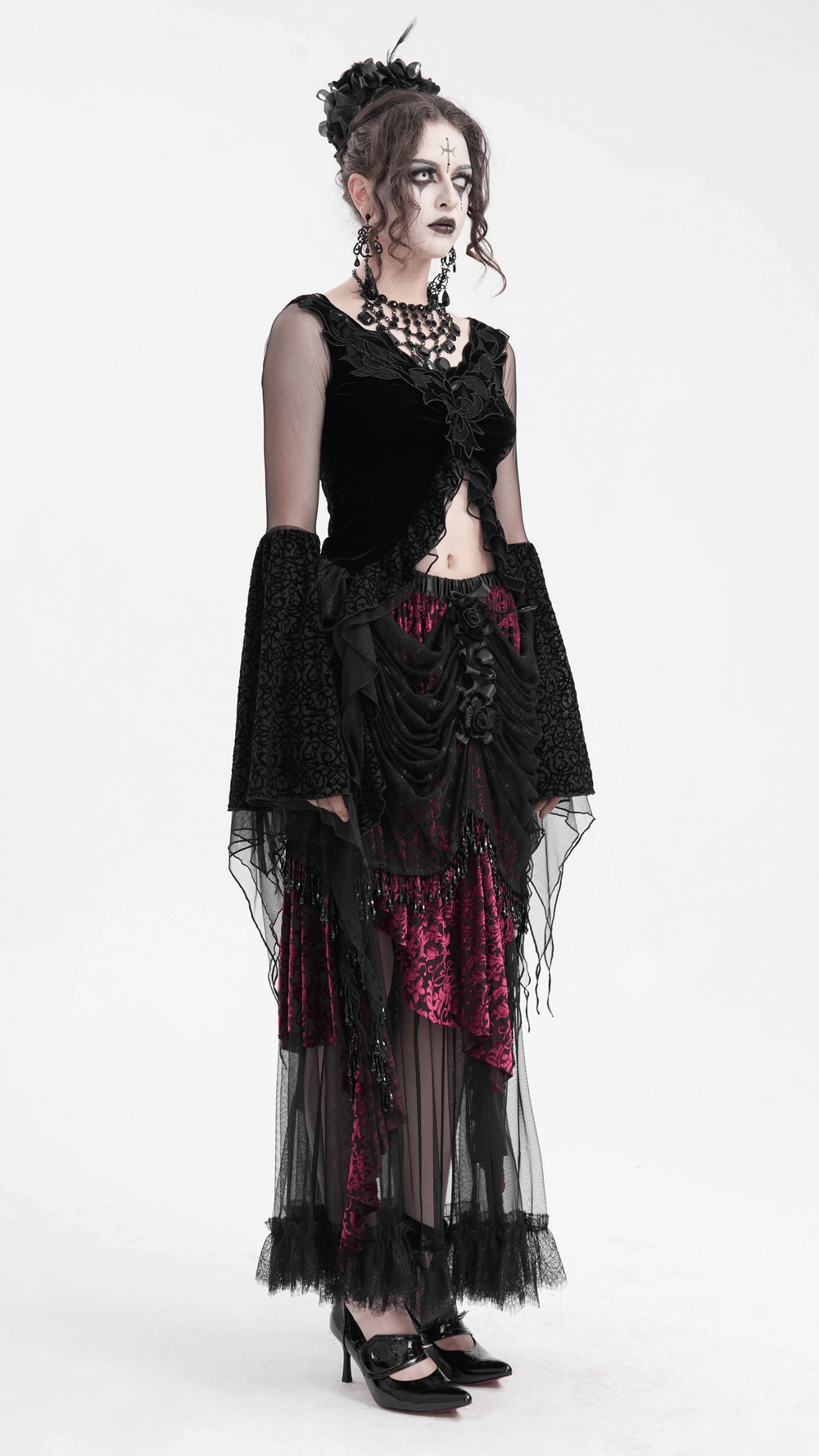 Model in a black gothic lace top with mesh sleeves and a flowing asymmetric hem, paired with dramatic skirt.