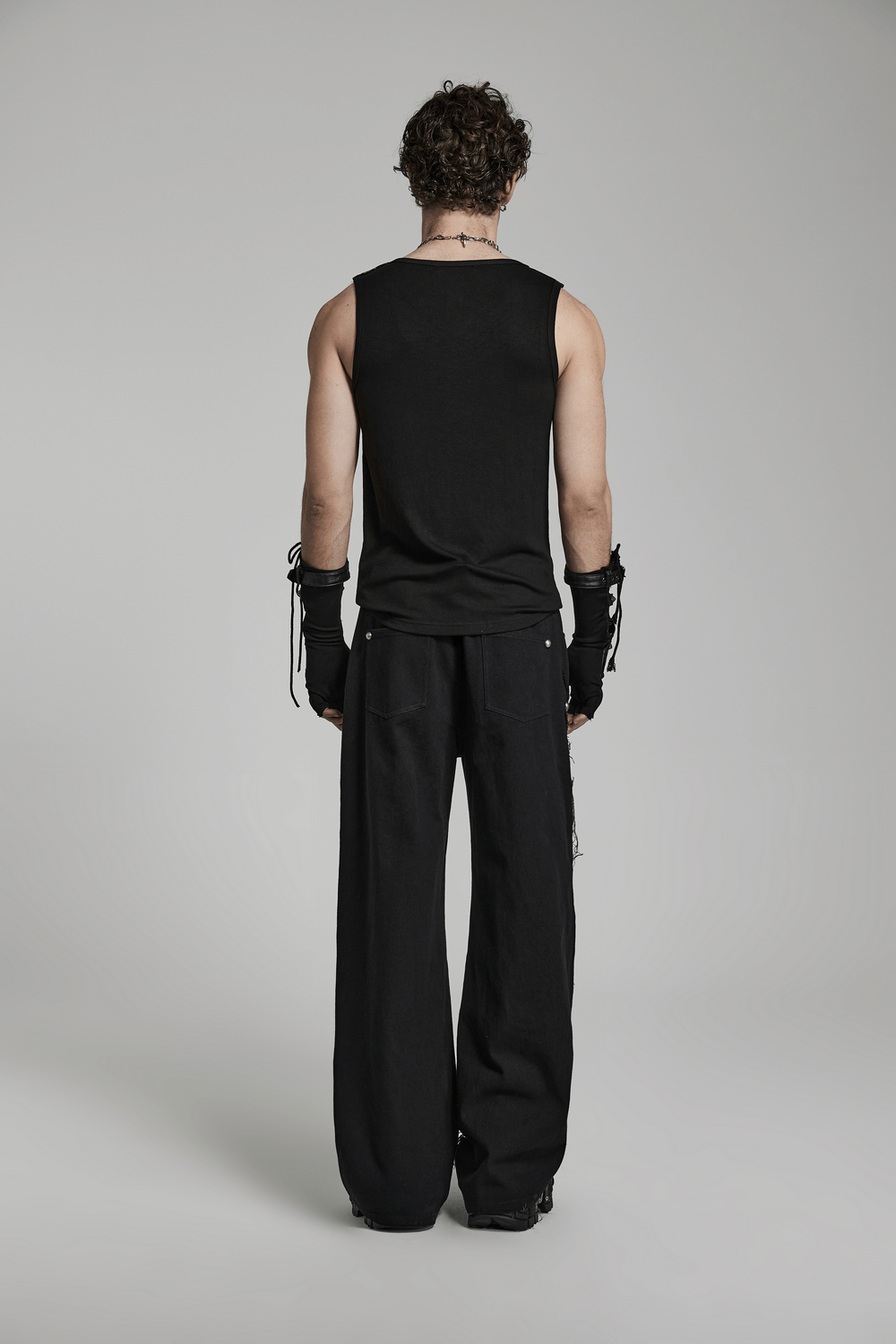 Man in sleeveless black top and black cargo pants with side ribbons, showcasing a gothic punk style from the back.