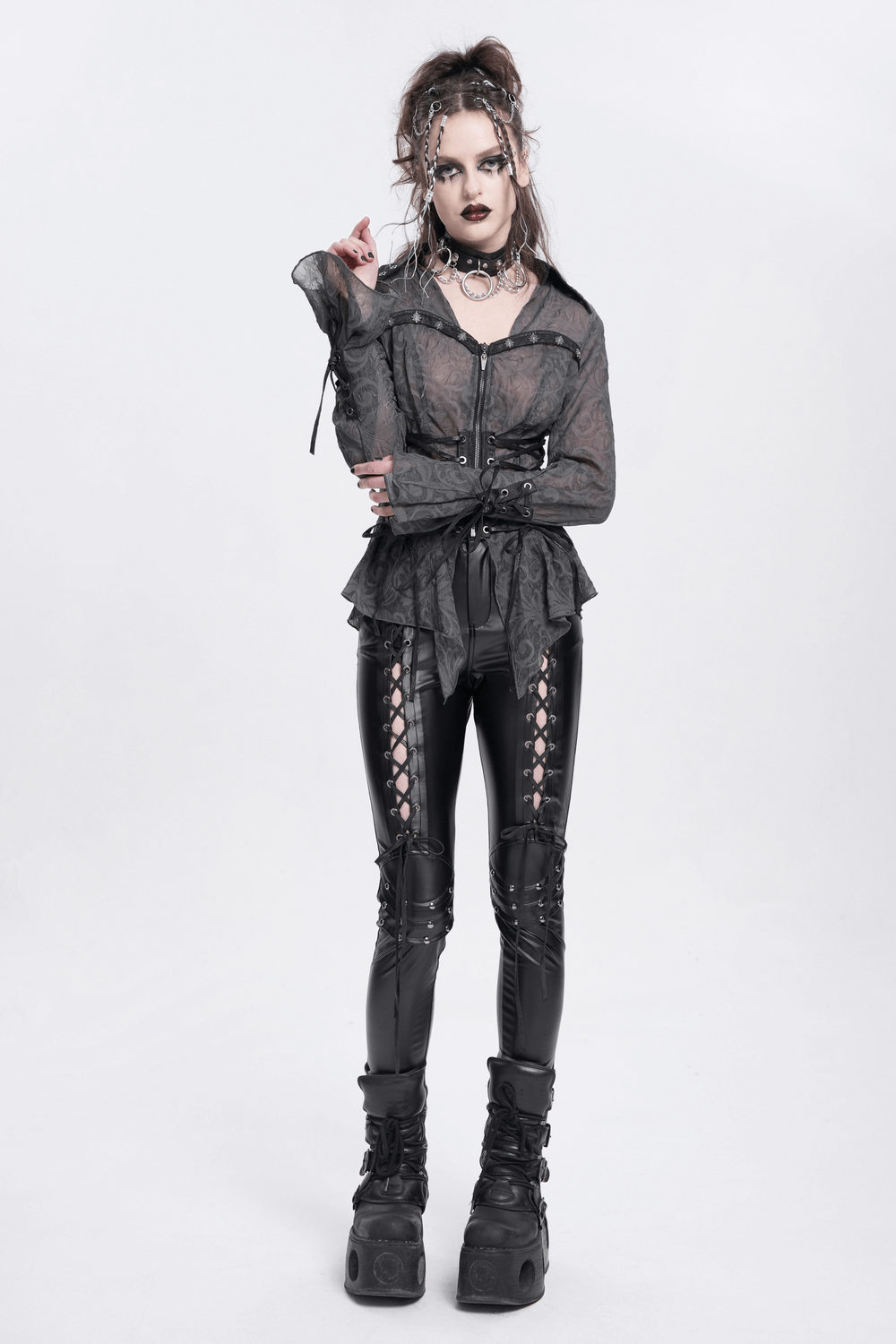 Model wearing black gothic lace-up pants with grommet details, paired with a sheer black top and platform boots.