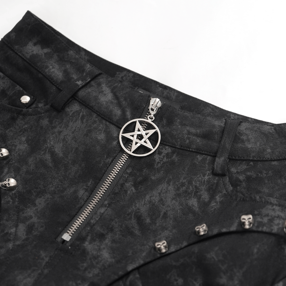 Close-up of black lace-up pants featuring a pentagram charm zipper and silver skull detailing for a gothic look.