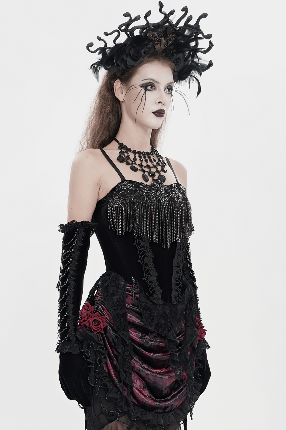 Alt Tag: Black Gothic Lace-Up Velvet Fringe Corset Top on model in dramatic gothic outfit with lace gloves, feathered headpiece, and fringed bodice