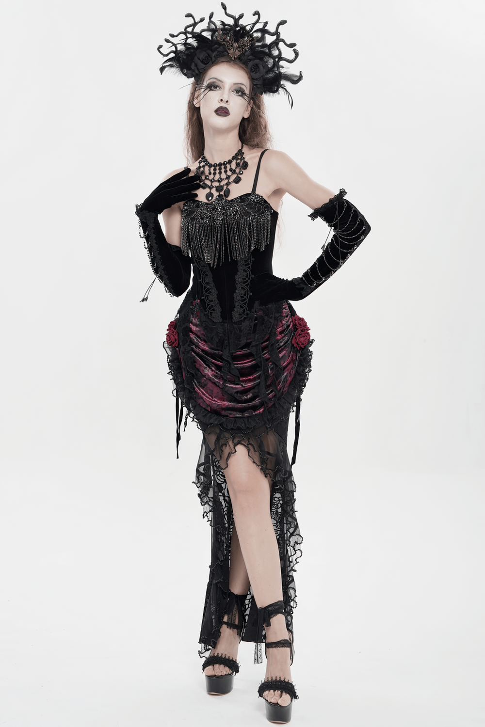 Alt Tag: Black Gothic Lace-Up Velvet Fringe Corset Top on model in dramatic gothic look, black lace skirt, statement headpiece, and heels