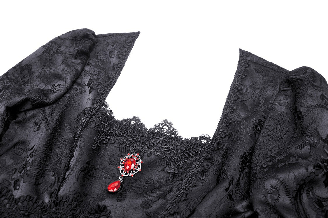 Close-up of a black lace maxi dress featuring a red statement brooch, showcasing Victorian elegance and intricate design.