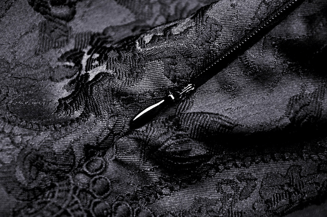 Close-up of black lace fabric with intricate pattern and zipper detail, highlighting gothic elegance.
