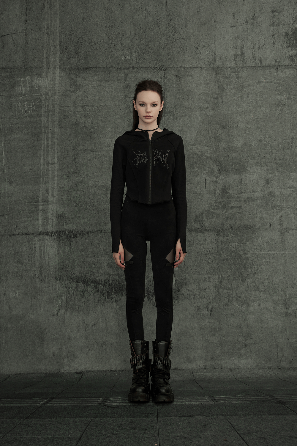 Model in black Gothic mesh-panel leggings with buckle accents, exuding edgy punk style in a minimalist concrete setting.