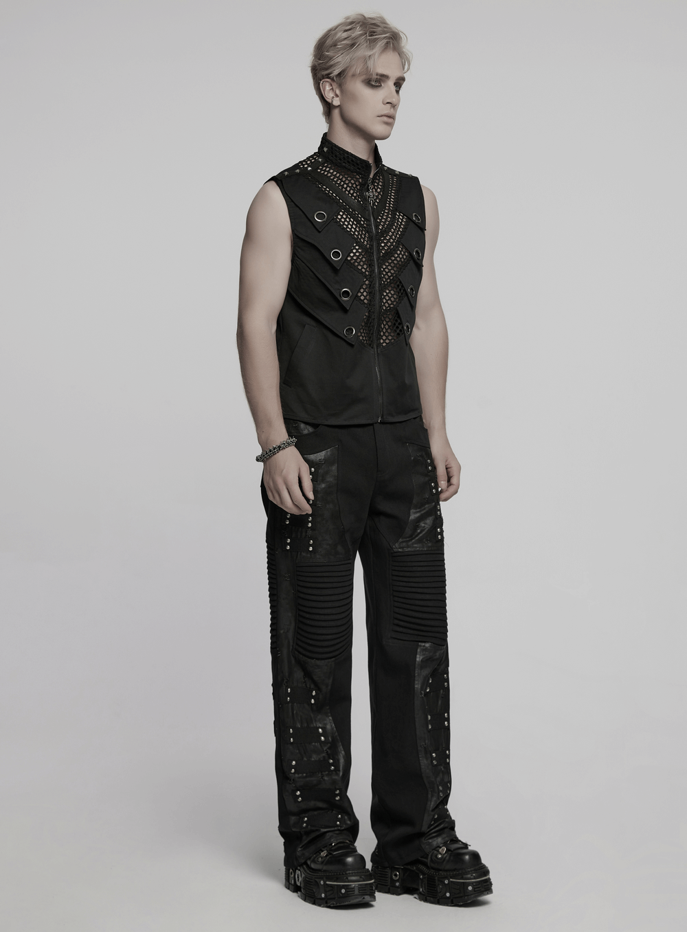 Model in black gothic pants with pleated panels, rivets, and a stylish sleeveless top, showcasing punk fashion.