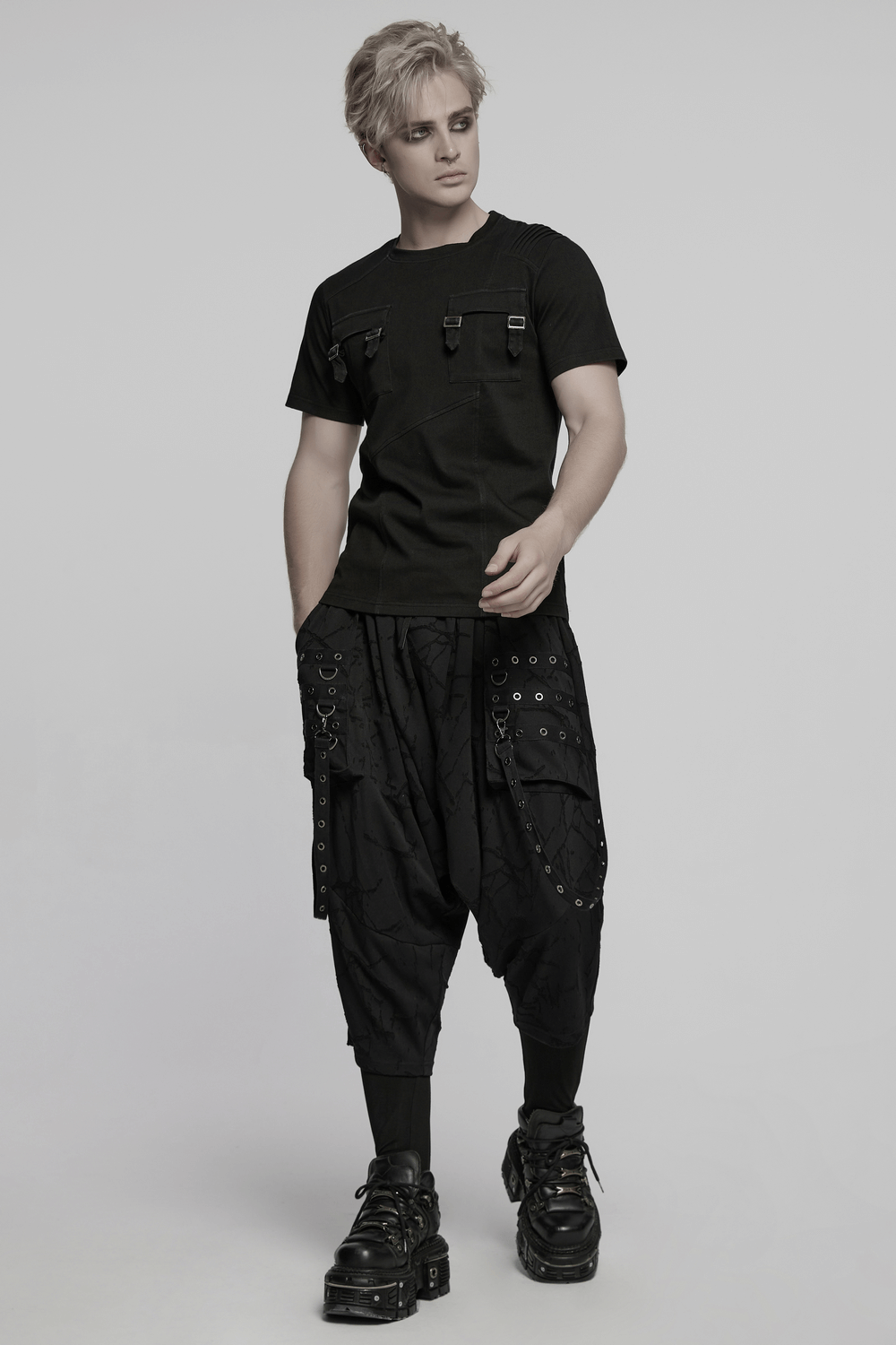 Model wearing a black gothic T-shirt with buckles, shoulder detail, and layered pants, showcasing punk style.