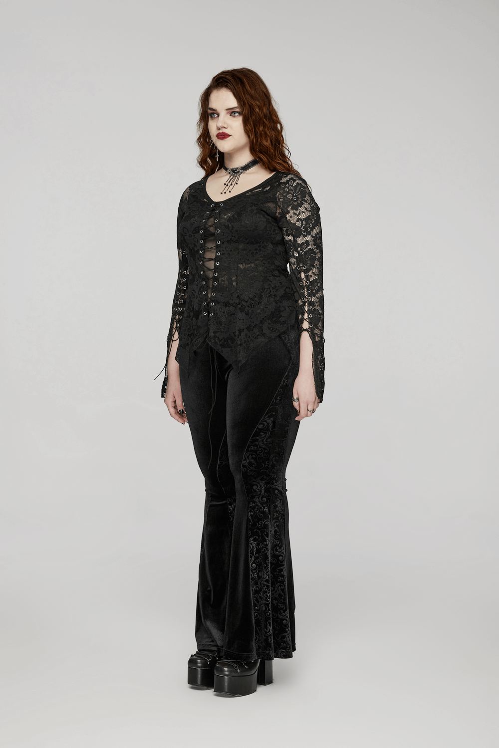 Model showcasing black gothic velvet flared pants with embossed detailing, paired with a lace top for a dramatic look.