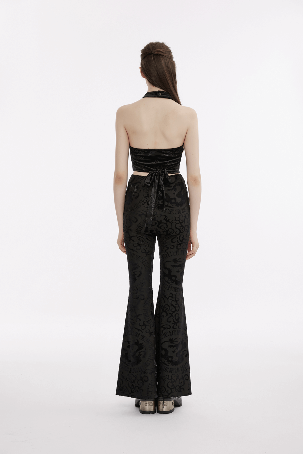 Model showcasing a back view of a black gothic velvet halter tank top with bow, styled with matching flared pants.
