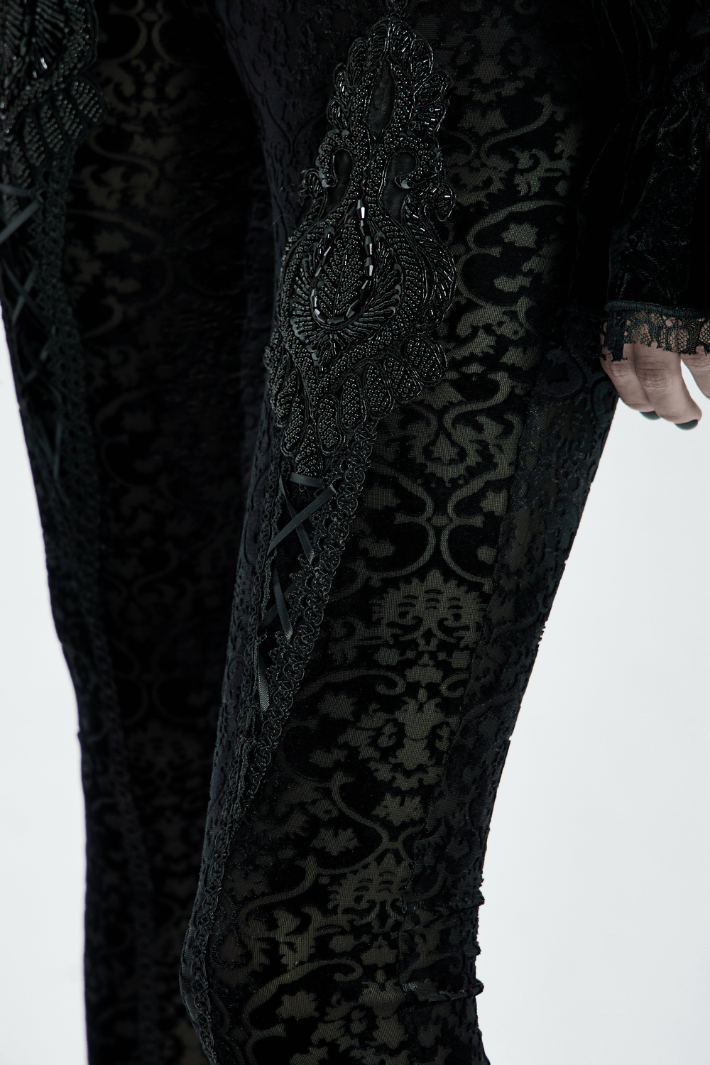 Close-up of black gothic velvet leggings with floral lace and intricate beadwork detailing.
